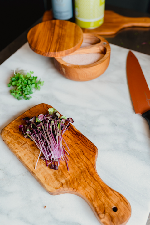 Grand Valley Micro Farms - Colorado - Cutting_board_radish Fresh microgreens on a wooden cutting board with a chef's knife, surrounded by a salt container and additional herbs, showcasing a modern kitchen setup.