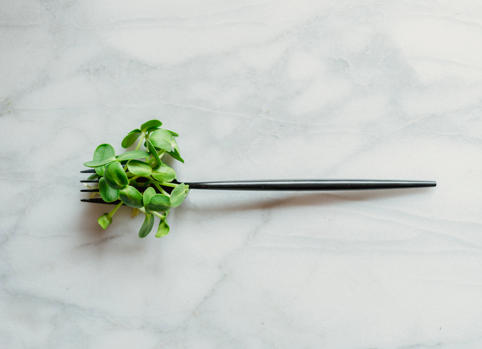 Black fork with fresh green microgreens resting on a marble surface, showcasing a modern culinary presentation.